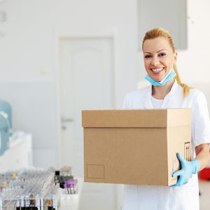 Attractive positive blond lab assistant carrying box with vaccines for Covid 19. Laboratory interior.